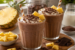 Twee glazen chocolade milkshakes gegarneerd met slagroom, chocoladeschaafsel en verse ananas, geserveerd op een houten plank met een halve ananas en chocolade ernaast
