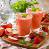 Twee glazen frisse aardbei appel sap met ijsblokjes, verse aardbeien en appelpartjes op een houten plank
