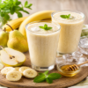 Romige banaan peer sap in twee glazen met banaan, peer, honing en ijsblokjes op tafel