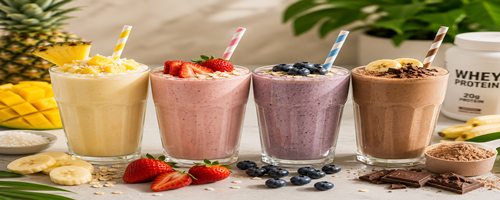 Vier glazen proteïne fruit milkshakes in verschillende smaken, gegarneerd met fruit en chocolade, met een pot whey proteïne op de achtergrond.
