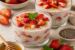 Glazen met aardbeien chia pudding, gevuld met verse aardbeienstukjes en afgewerkt met munt, omringd door aardbeien, amandelen en chiazaad.