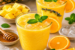 Twee glazen ananas-sinaasappel vitamine boost sap met munt als garnering, omringd door ananasstukjes, sinaasappelpartjes, honing en ijsblokjes.