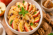 Gezonde appelsalade met verse rode appelpartjes, walnoten, rozijnen, honing en kaneel in een kom. Voedzaam ontbijt, gezonde snack of dessert met fruit en noten.