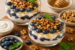 Yoghurt parfait met blauwe bessen, walnoten, honing en munt in glazen dessertcups. Eiwitrijk ontbijt met vers fruit, yoghurt en gezonde toppings.