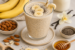 Romige chia-banaan milkshake met bananenschijfjes, geserveerd naast amandelen, chiazaad, honing, melk en vanille.