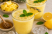 Twee glazen citroen-sinaasappel vitamine boost sap, afgewerkt met verse munt en geserveerd met ananas, citrusvruchten, honing en ijsblokjes.