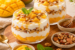 Romige yoghurt parfait met verse mango, gemengde noten, honing en munt in glazen. Gezond ontbijt of dessert met tropisch fruit en natuurlijke ingrediënten.
