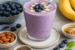 Romige blauwe bessen milkshake met banaan, gegarneerd met verse blauwe bessen, geserveerd naast amandelen, chiazaad en honing.