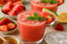 Twee glazen watermeloen-aardbei vitamine boost sap, gegarneerd met verse munt, geserveerd met stukjes watermeloen, aardbeien, citruspartjes, honing en ijsblokjes.